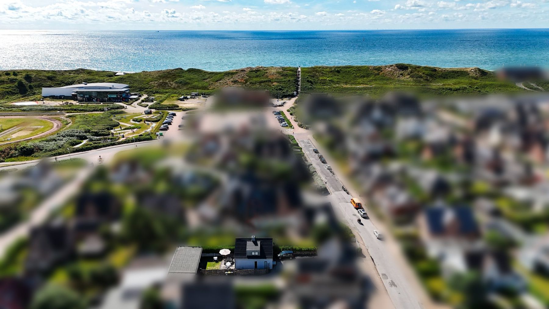 Luftaufnahme einer Wohnsiedlung mit Straße und Blick auf das Meer im Hintergrund.