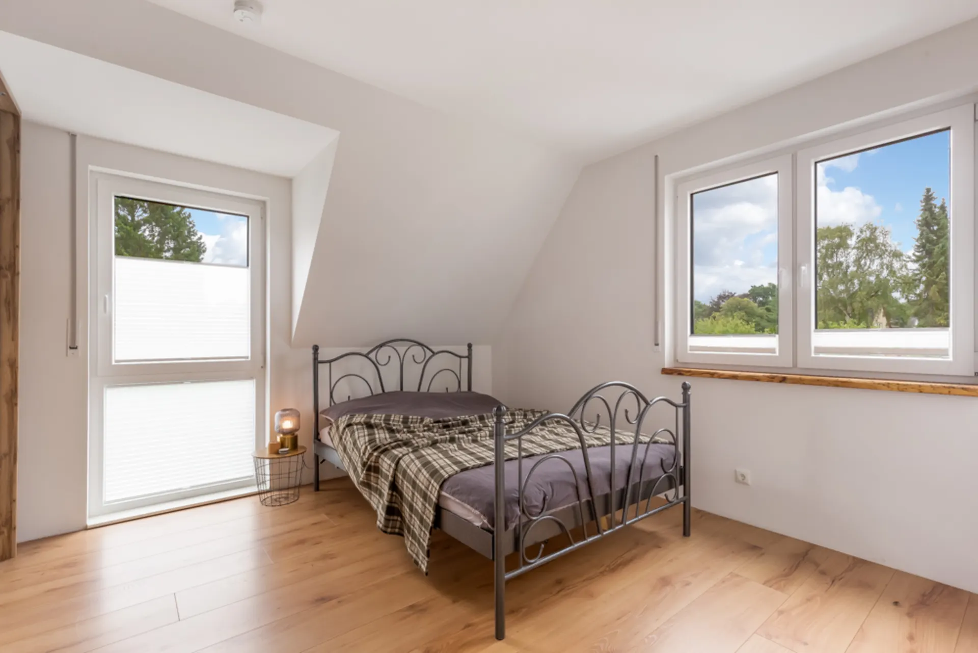 Helles Schlafzimmer mit Einzelbett, Holzboden und großen Fenstern, Blick nach draußen.