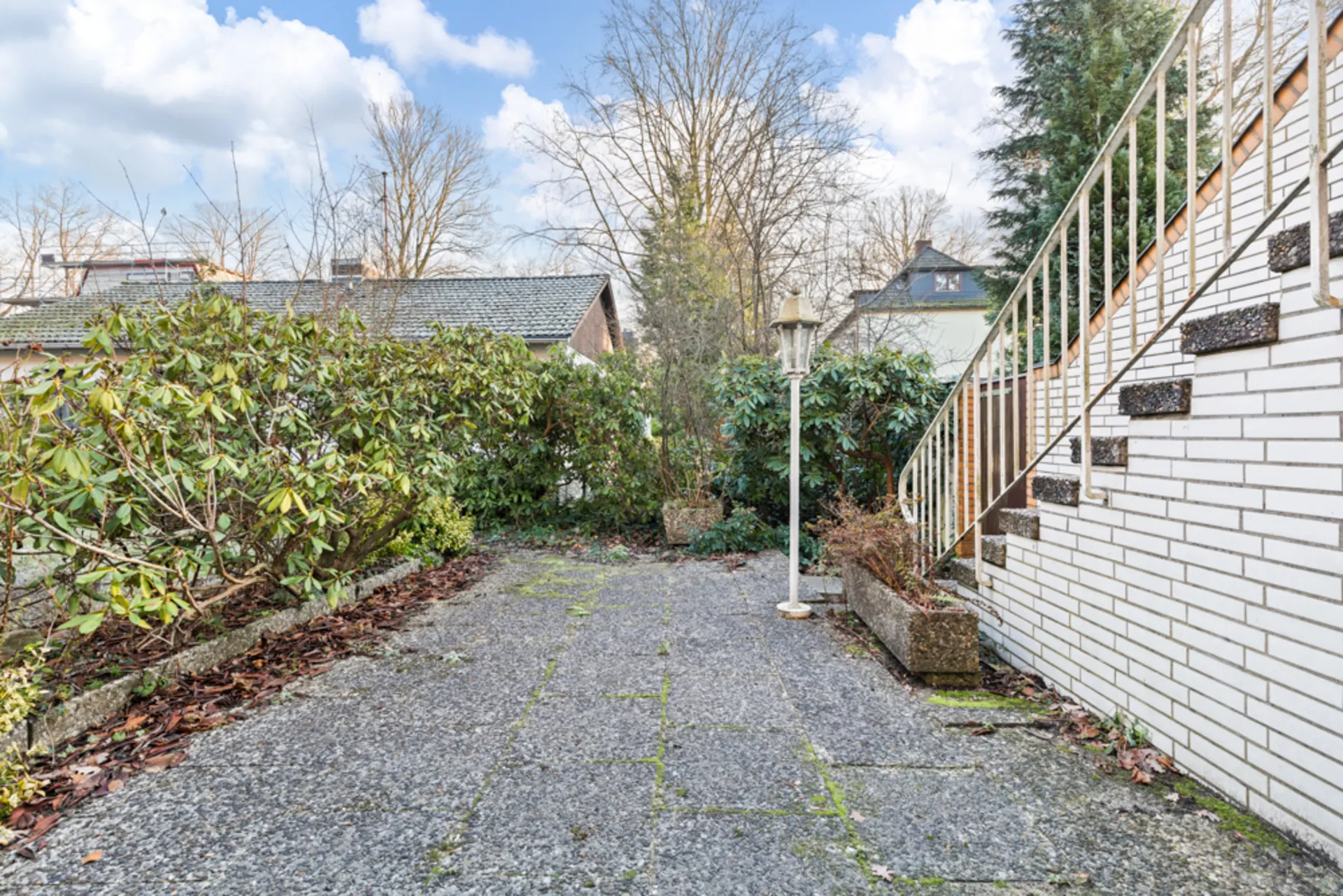 Gepflasterte Terrasse mit Treppe, weißen Ziegeln und grünen Sträuchern im Garten.