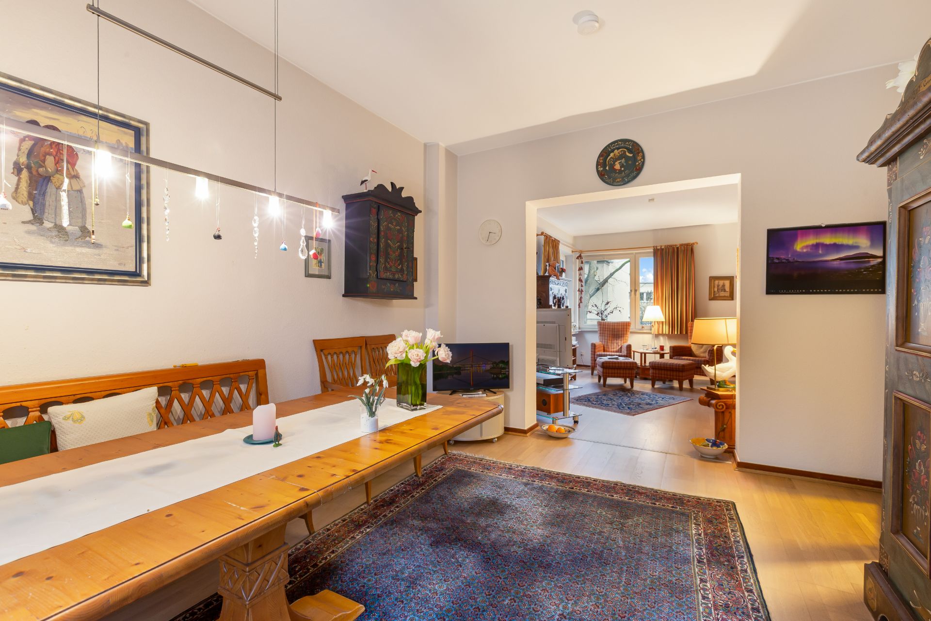 Esszimmer mit Holzbank und Tisch, angrenzend an ein Wohnzimmer mit Sofa und großem Fenster.