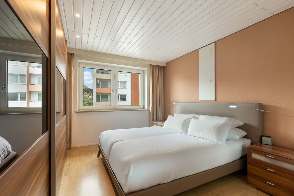 Modernes Schlafzimmer mit Doppelbett, zwei Nachttischen und großem Fenster.