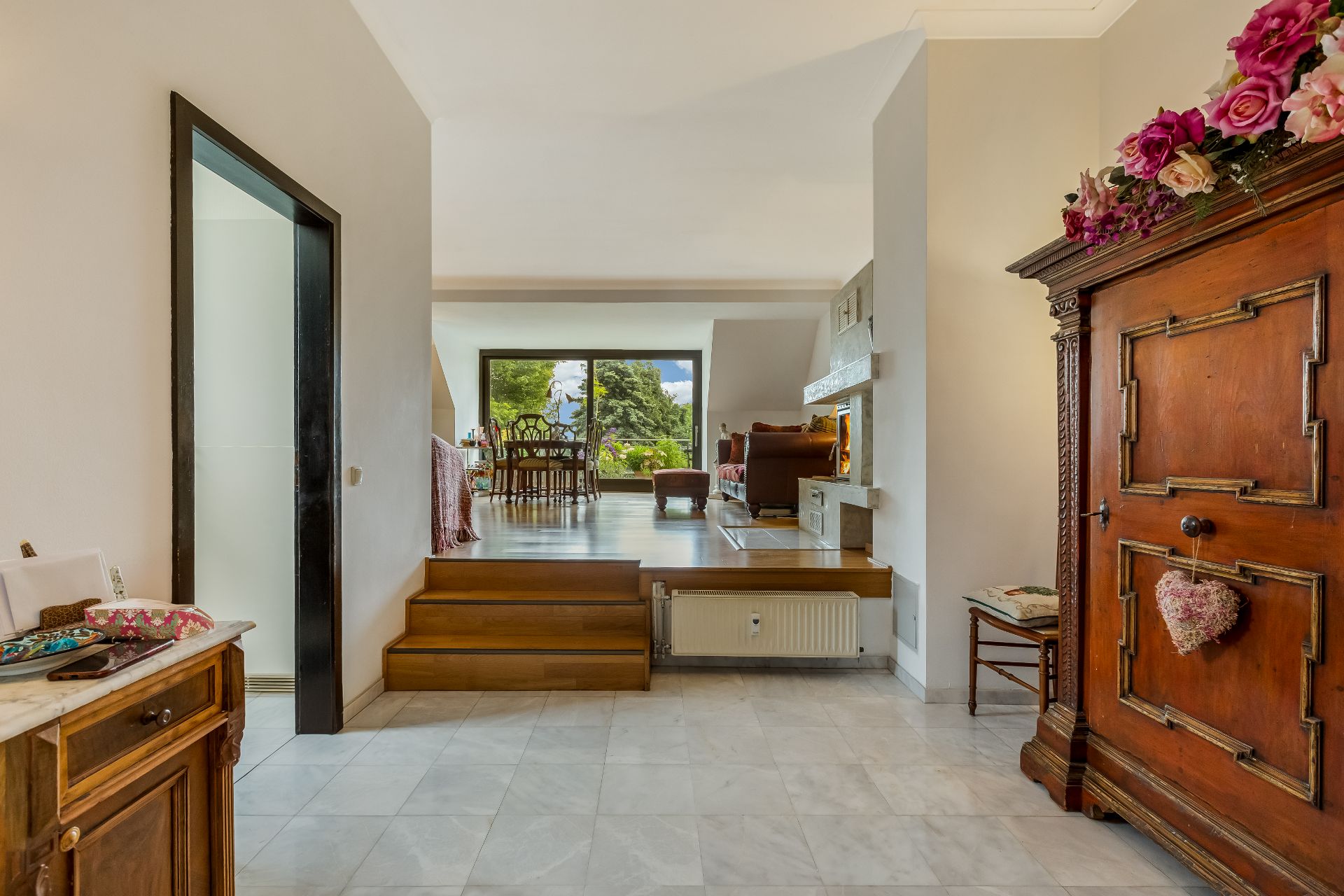 Eingangsbereich mit Blick ins Wohnzimmer, Holzschrank und Stufen zum Essbereich.