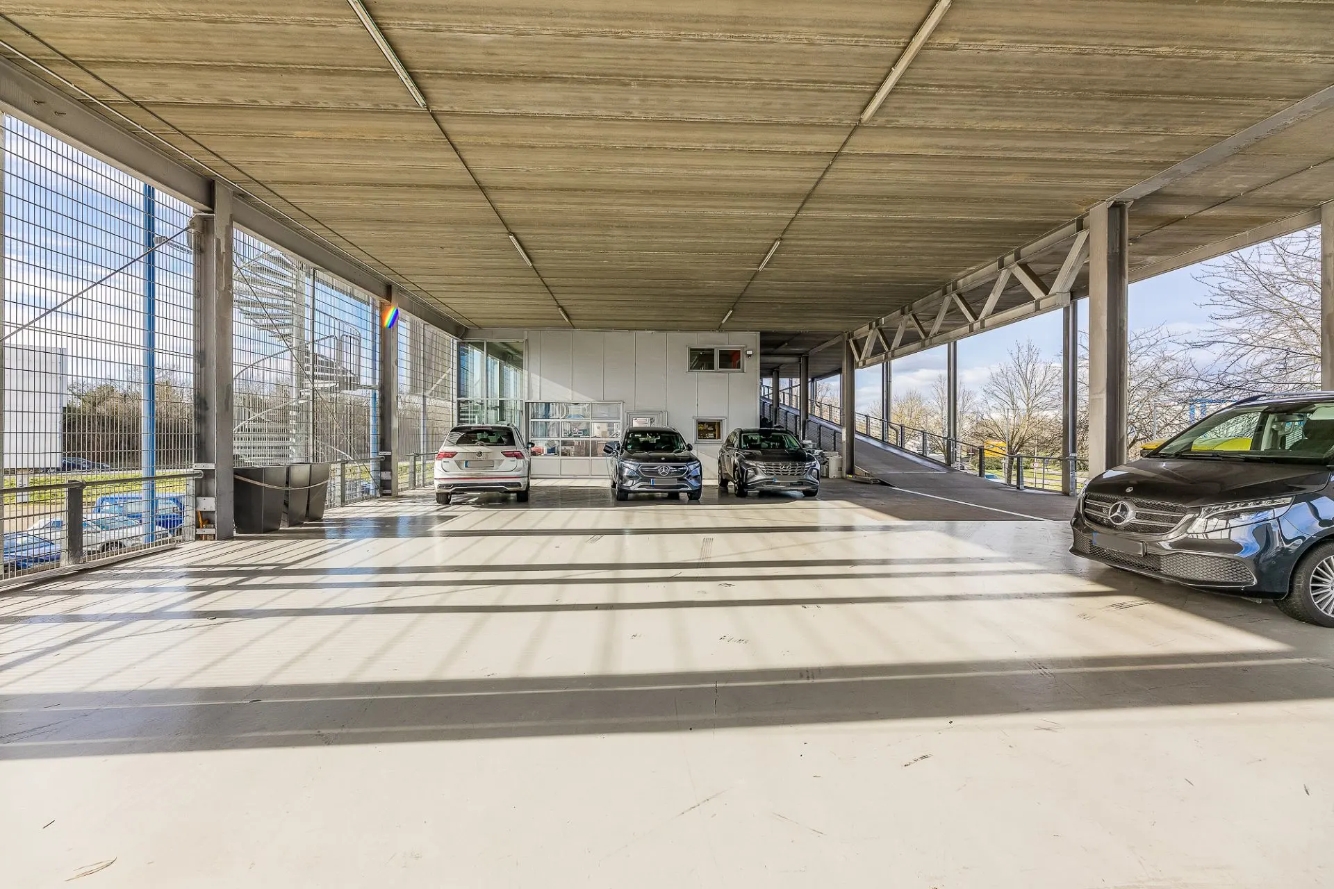 Offene, überdachte Parkfläche mit mehreren geparkten Autos und verglasten Seitenwänden.
