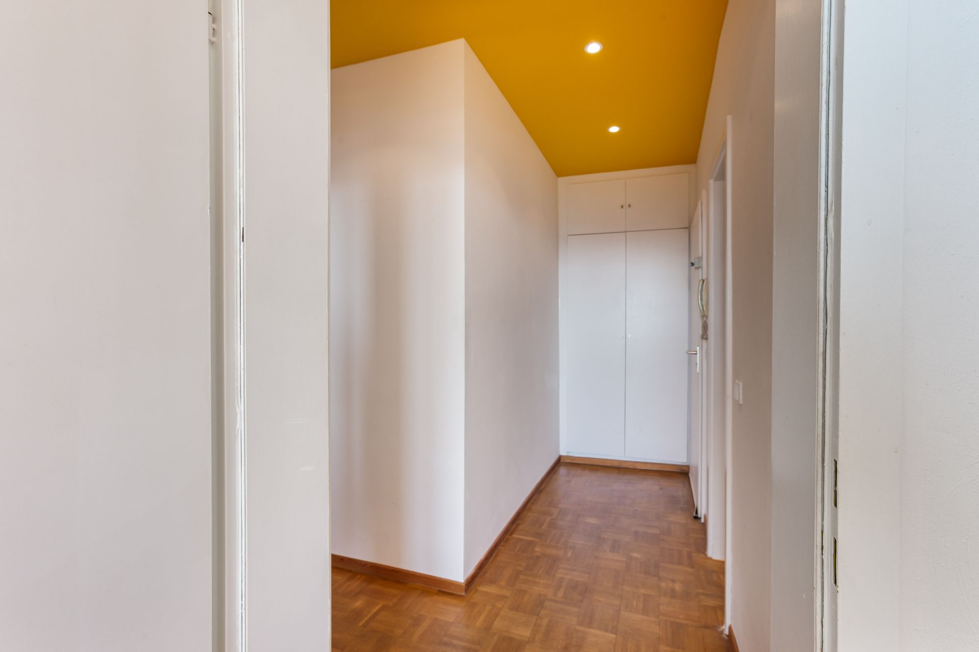 Flur mit gelber Decke, weißem Wandschrank und Parkettboden.