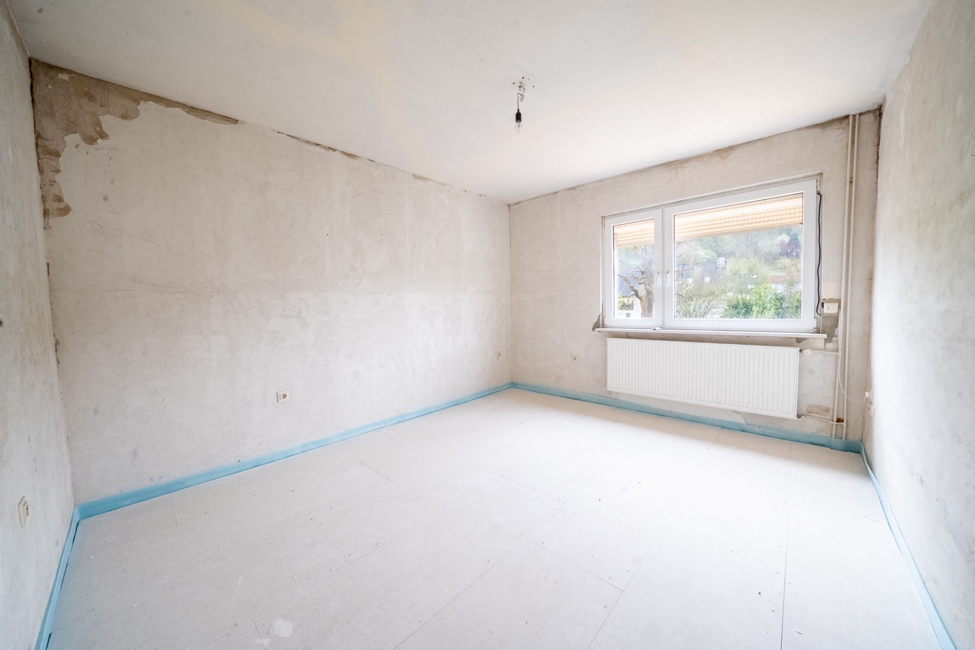 Leerer Raum mit weiß gestrichenen Wänden, großem Fenster und sichtbarem Heizkörper.