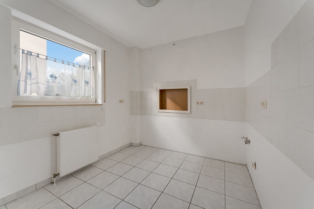 Leerer, gefliester Raum mit Fenster, Heizung und Wandöffnung.