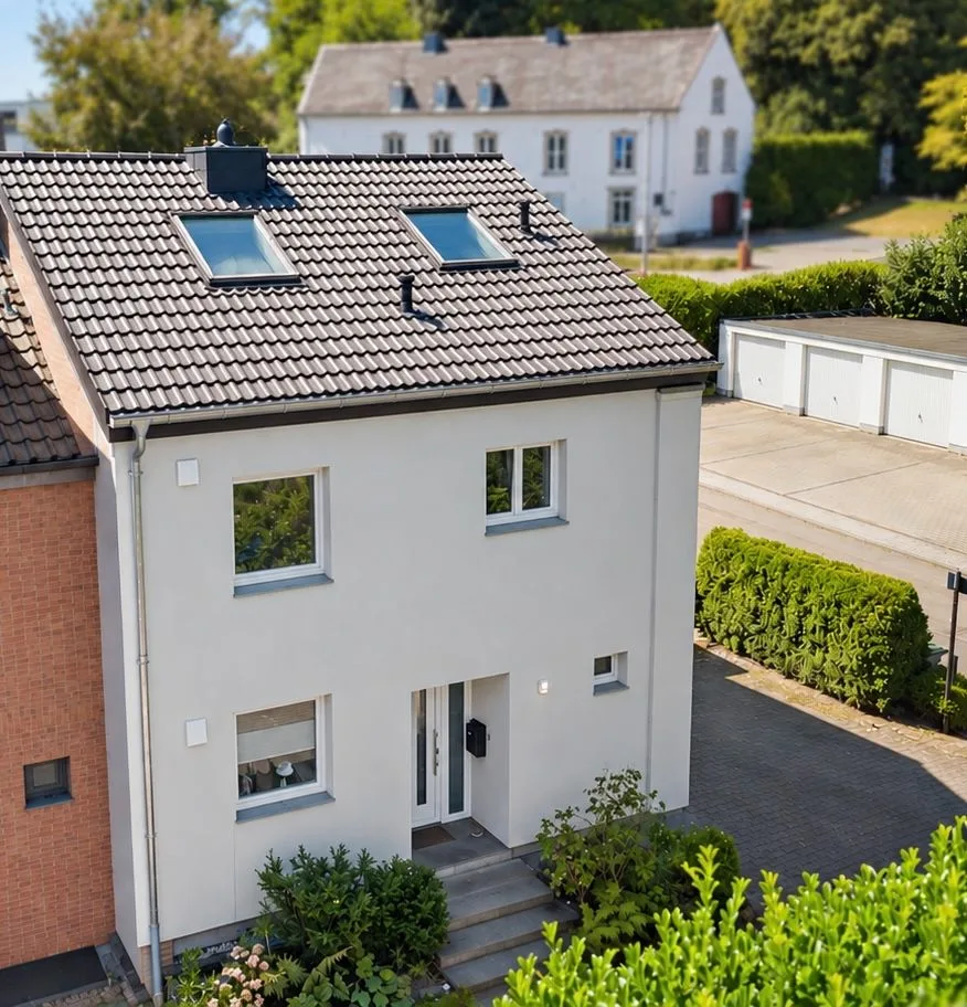 Modernes, zweistöckiges Wohnhaus mit grauem Dach und Vorgarten, daneben Garagen.