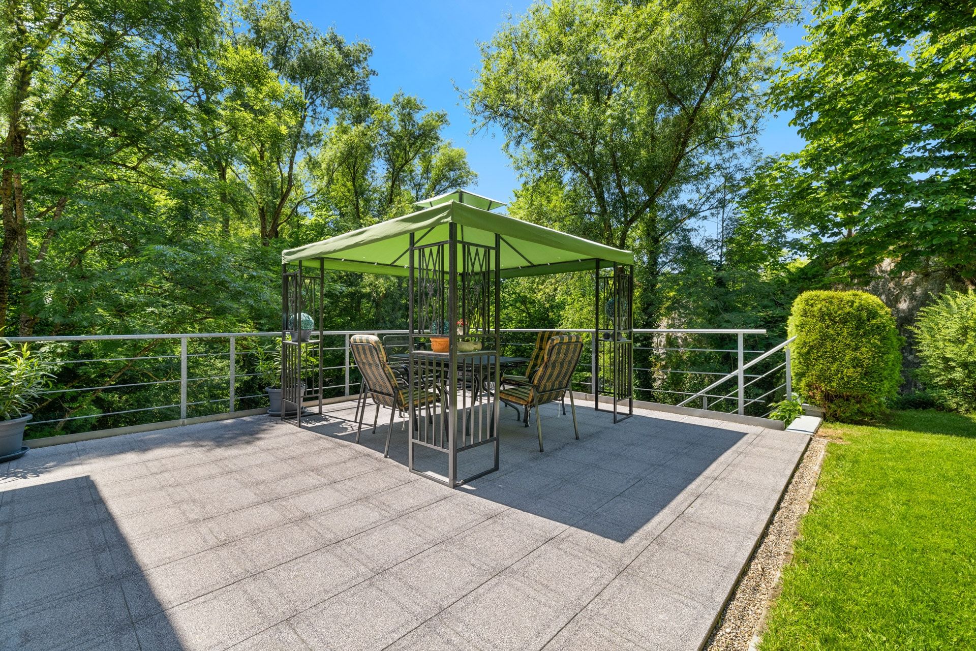 Terrasse mit grünem Pavillon, Tisch und Stühlen, umgeben von Bäumen und Rasen.