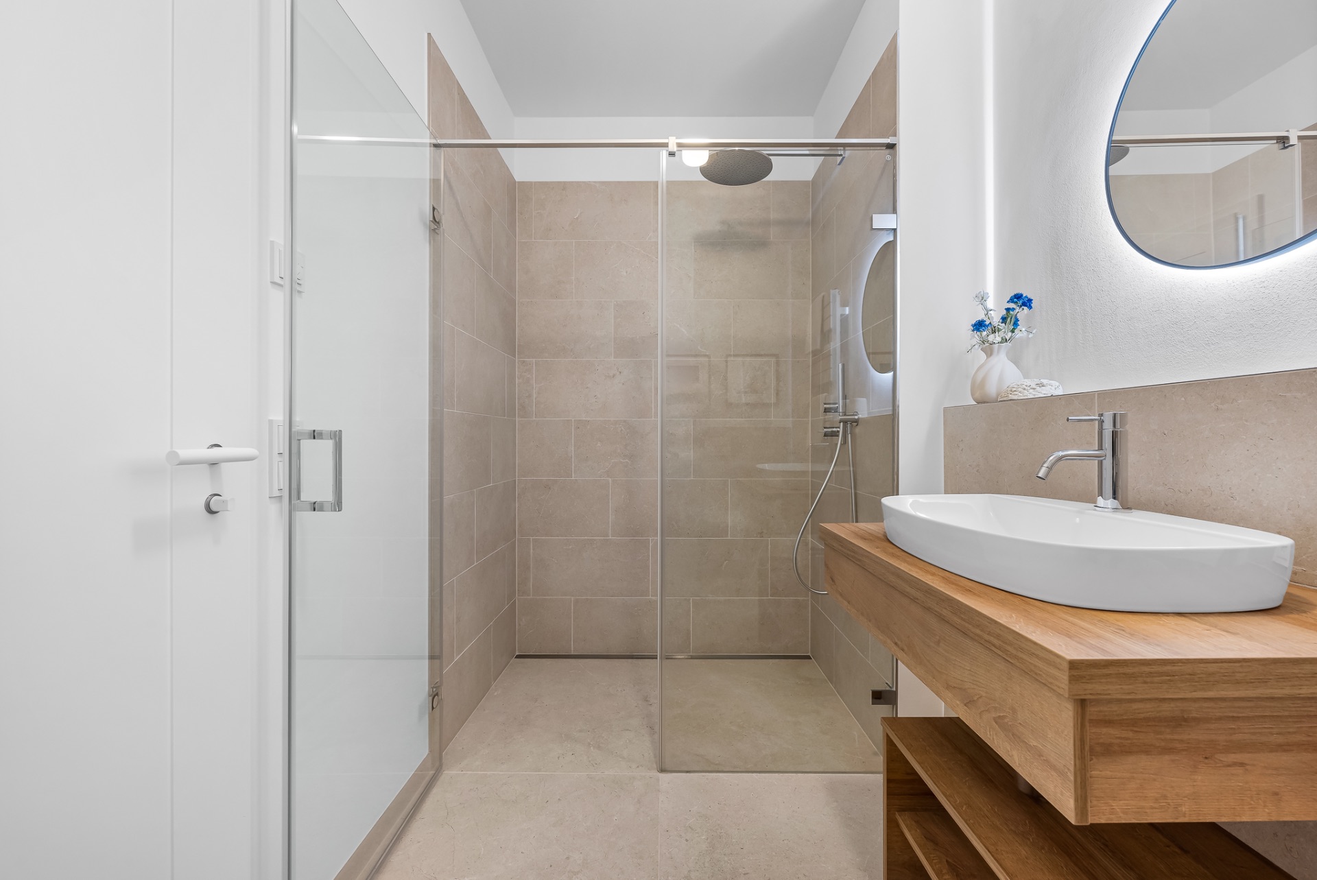 Modernes Badezimmer mit großer begehbarer Dusche, Holzwaschtisch und ovalem Spiegel.