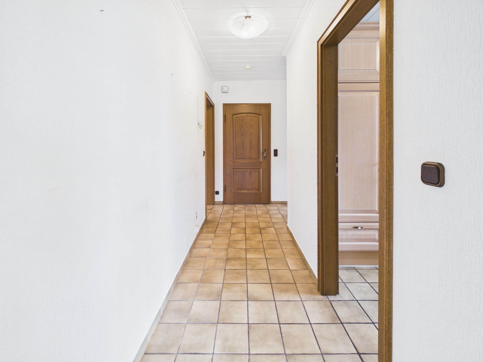 Heller Flur mit Fliesenboden, weißen Wänden und Holztüren in einer Wohnung.