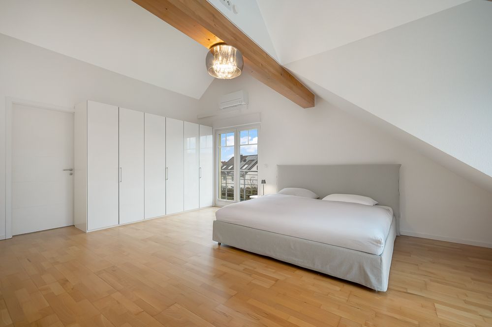 Helles Schlafzimmer mit Doppelbett, Kleiderschränken und Holzboden unter Dachschräge.