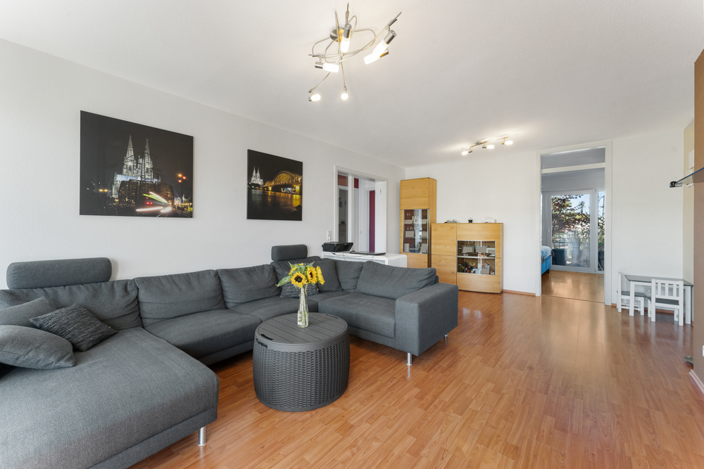 Wohnzimmer mit grauem Ecksofa, Holzboden, runder Couchtisch mit Sonnenblumen und Wandbildern.