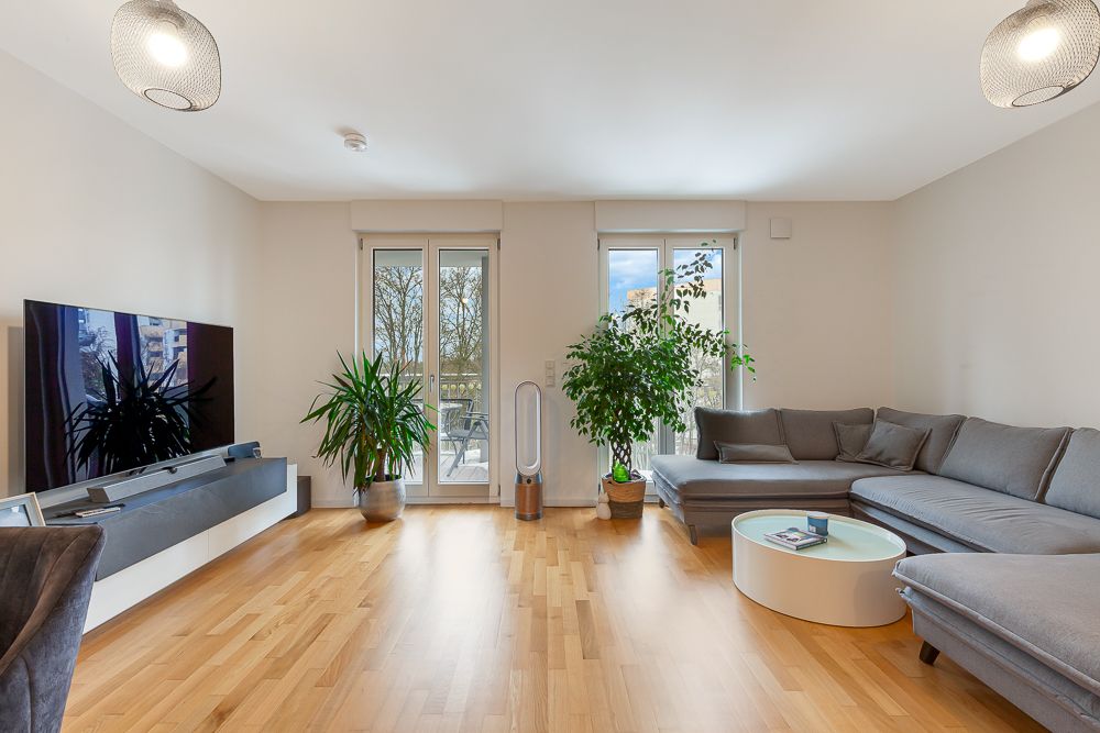 Modernes Wohnzimmer mit grauem Ecksofa, Flachbildfernseher, Holzboden und Zimmerpflanzen.