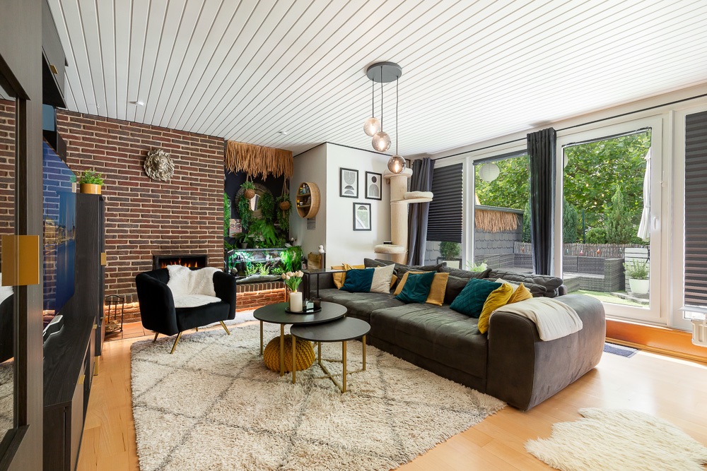 Modernes Wohnzimmer mit großer Eckcouch, Teppich, Couchtisch und großen Fenstern zum Garten.
