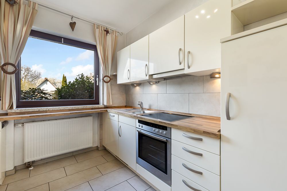 Helle Küche mit Holzarbeitsplatten, weißen Schränken und großem Fenster mit Blick ins Grüne.