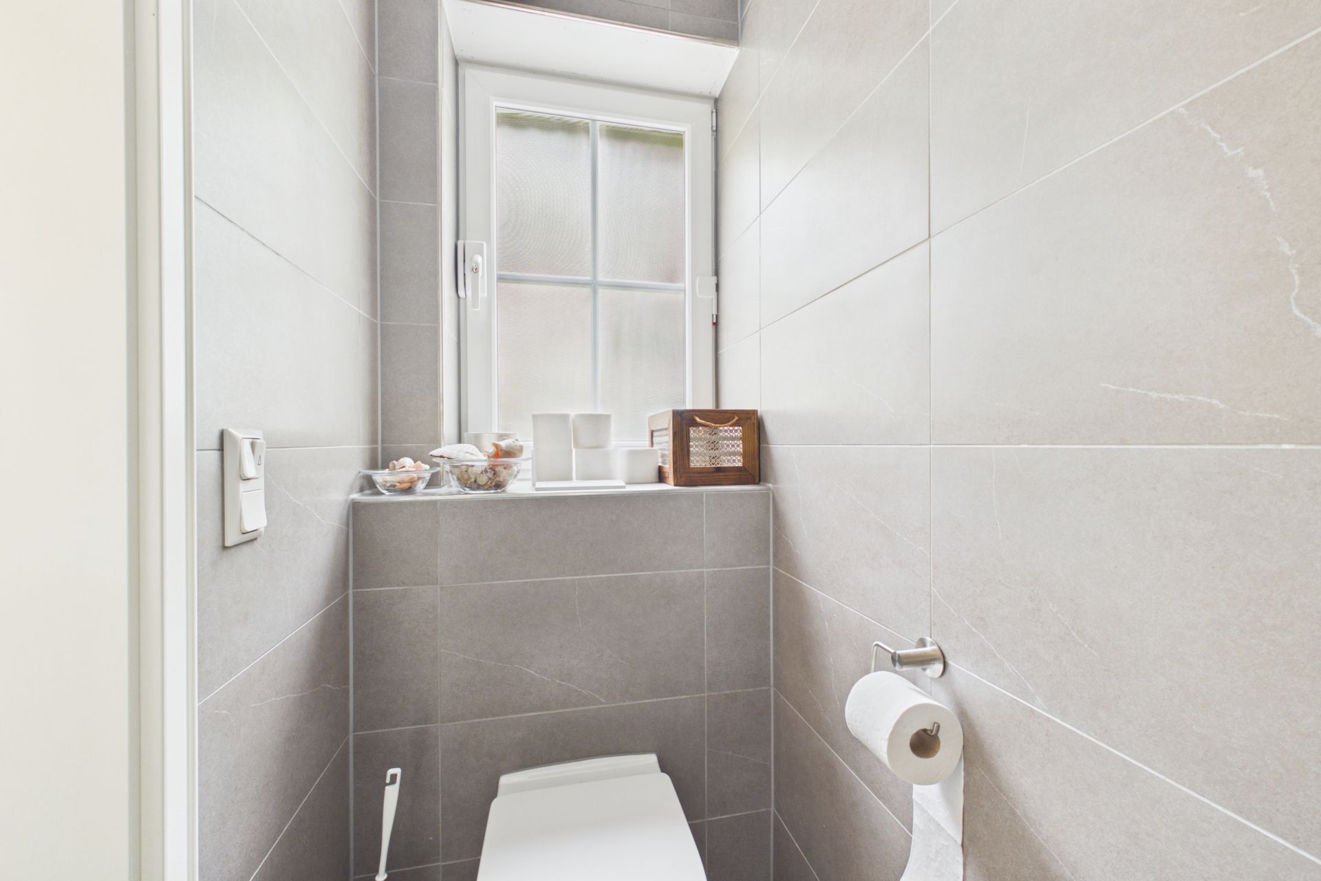 Kleines Badezimmer mit Toilette, Papierrolle und Fenster, Dekor auf der Fensterbank.