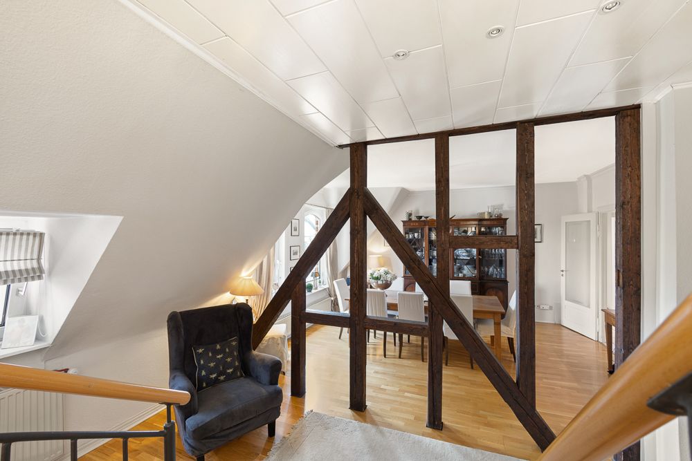 Wohnzimmer mit Essbereich, Holzdecke, urigen Holzbalken und Sessel neben Fenster.
