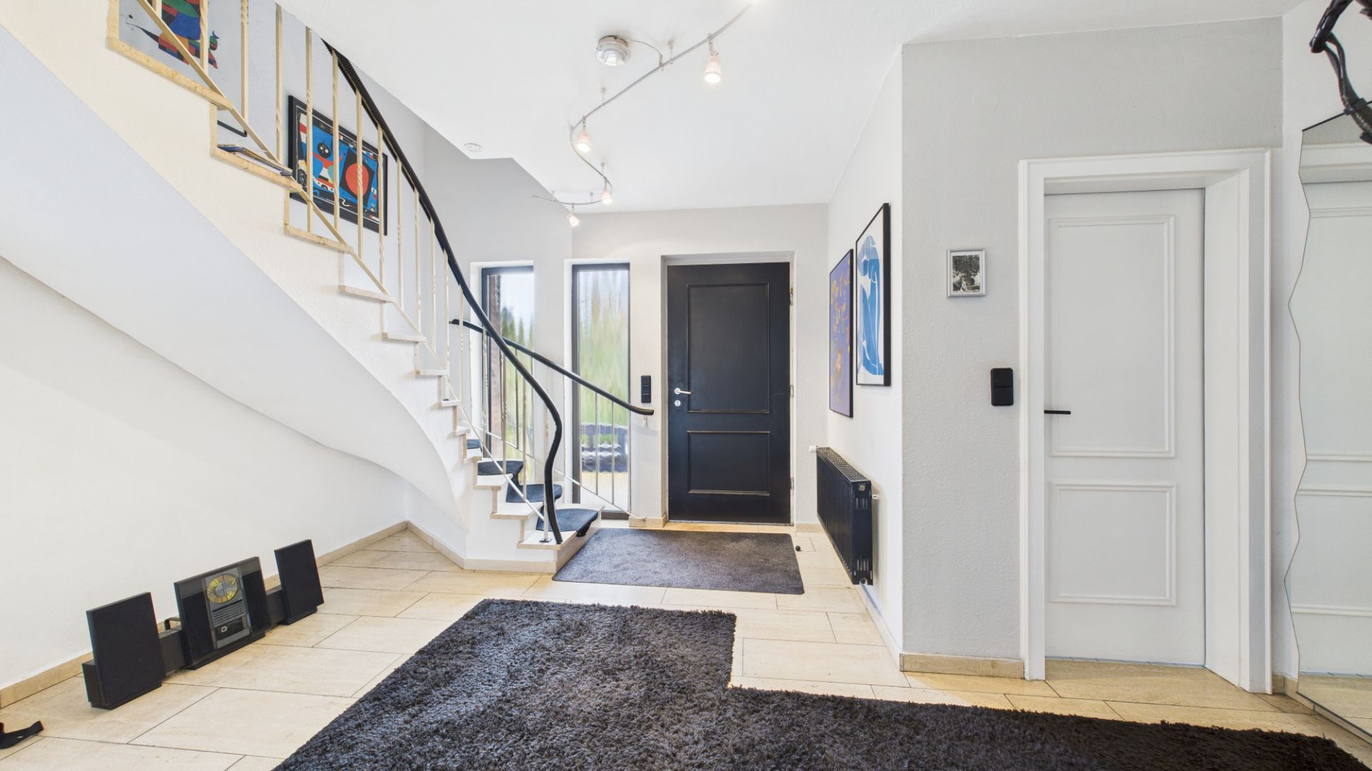 Heller Flur mit schwarzer Tür, Treppe, Teppich und Wandbildern.