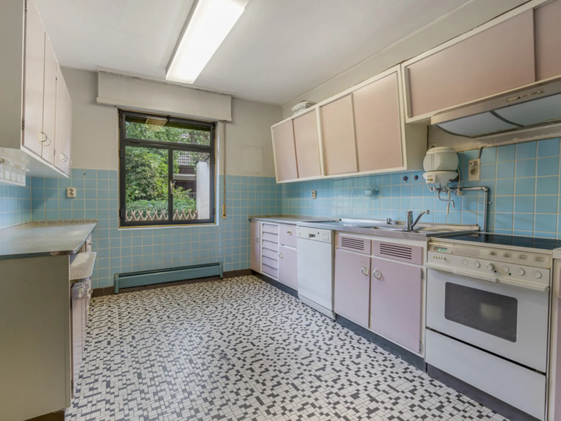 Helle Küche mit rosa Schränken, blau gefliesten Wänden und großem Fenster.