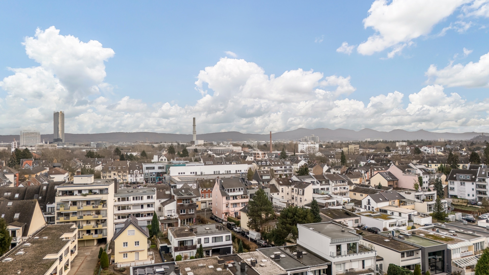 Blick auf ein Wohnviertel mit vielen Häusern und Bergen im Hintergrund unter blauem Himmel.
