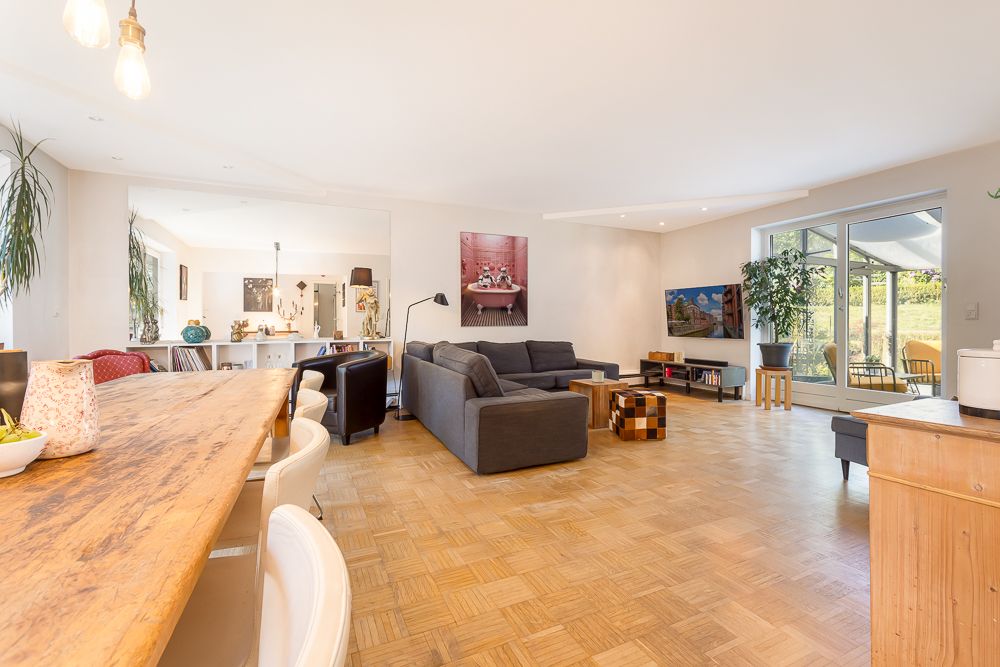 Helles Wohnzimmer mit großem Holztisch, grauem Sofa und Zugang zur Terrasse.