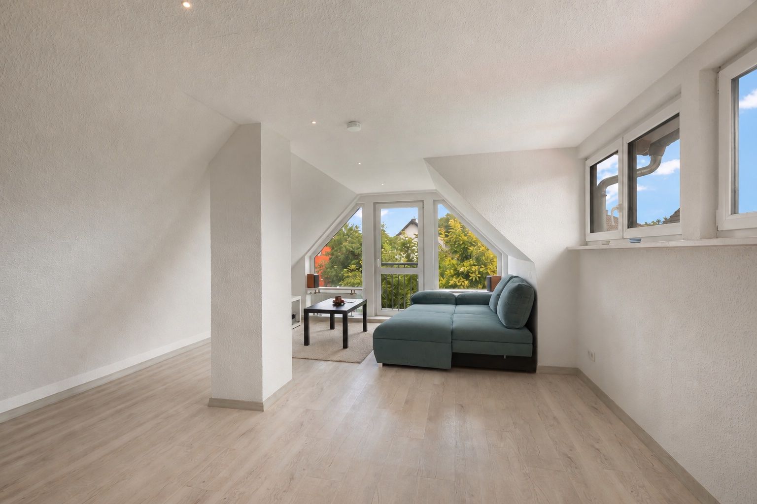 Helles Wohnzimmer mit Ecksofa, Couchtisch und großen Fenstern unter Dachschrägen.