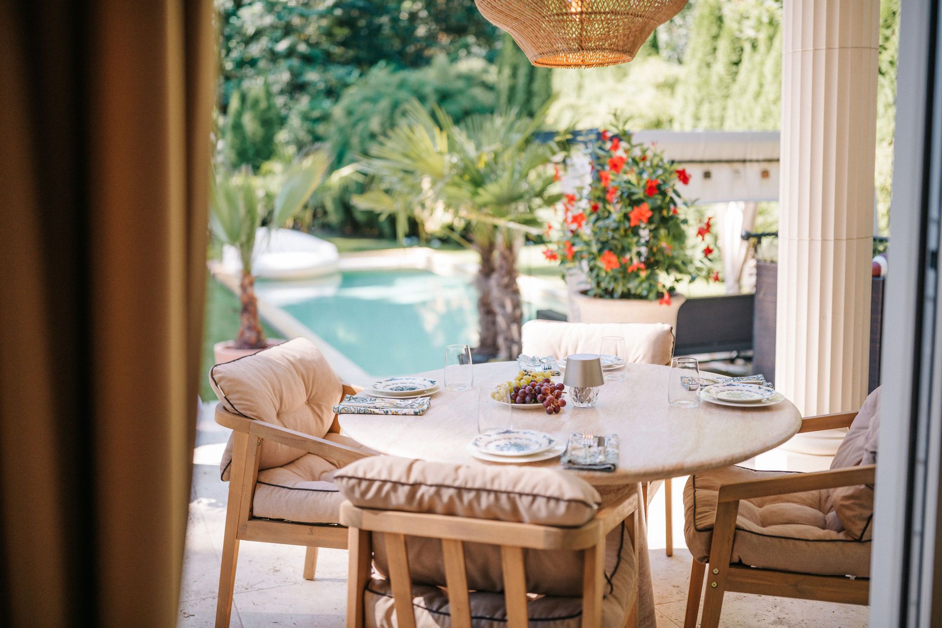 Runder Tisch mit vier Stühlen auf Terrasse, gedeckt, Blick auf Pool und Garten.