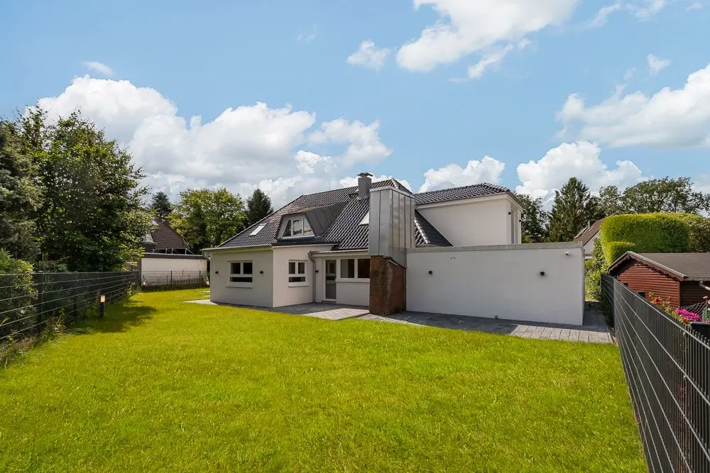 Modernes Einfamilienhaus mit Garten, Terrasse und Zaun bei sonnigem Wetter.