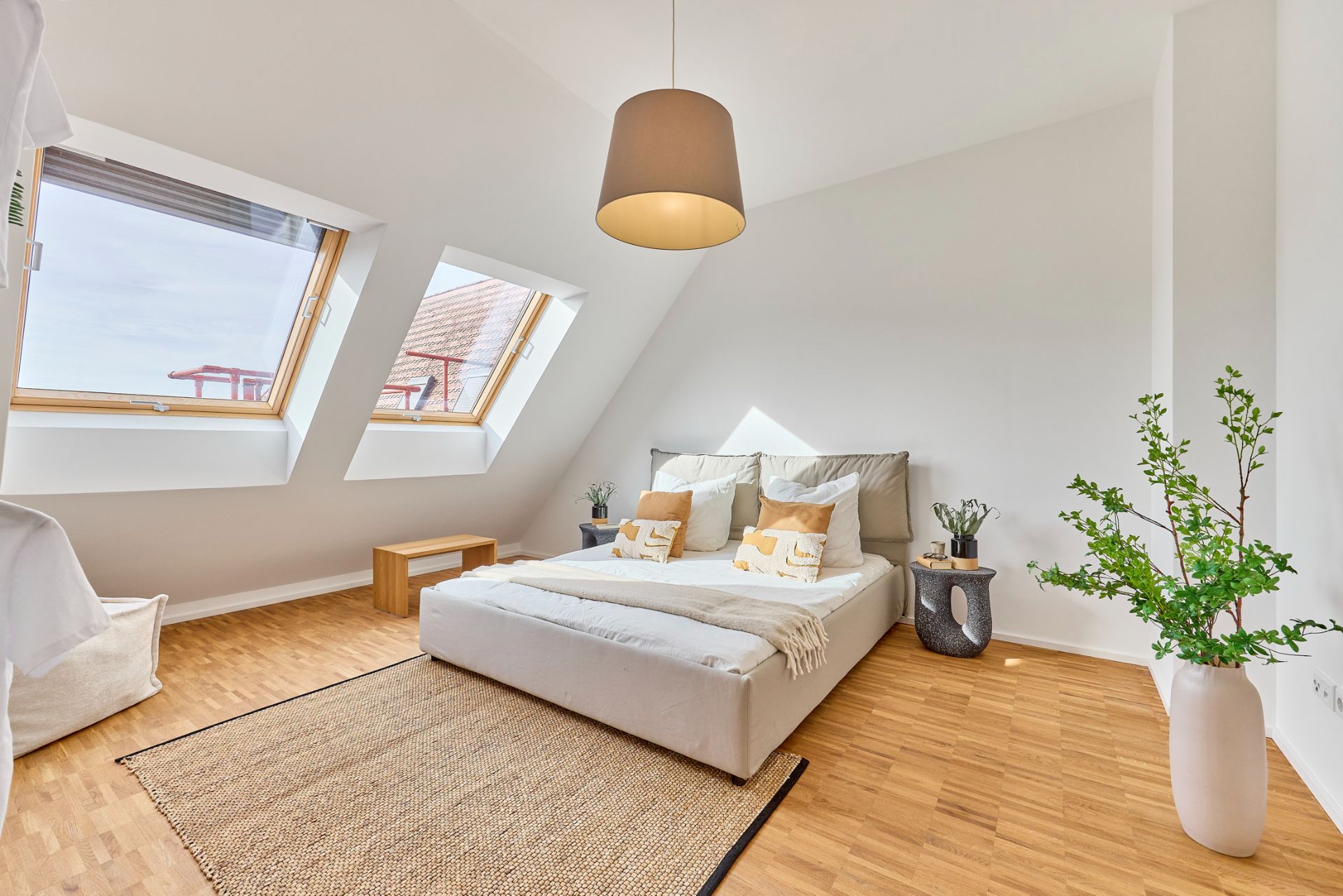 Helles Schlafzimmer mit Doppelbett, Holzboden, großen Fenstern und einer Pflanze in einer weißen Vase.