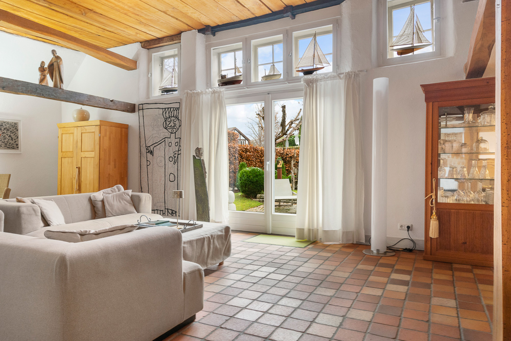 Helles Wohnzimmer mit Sofa, großen Fenstern, Vitrine und Blick in den Garten.