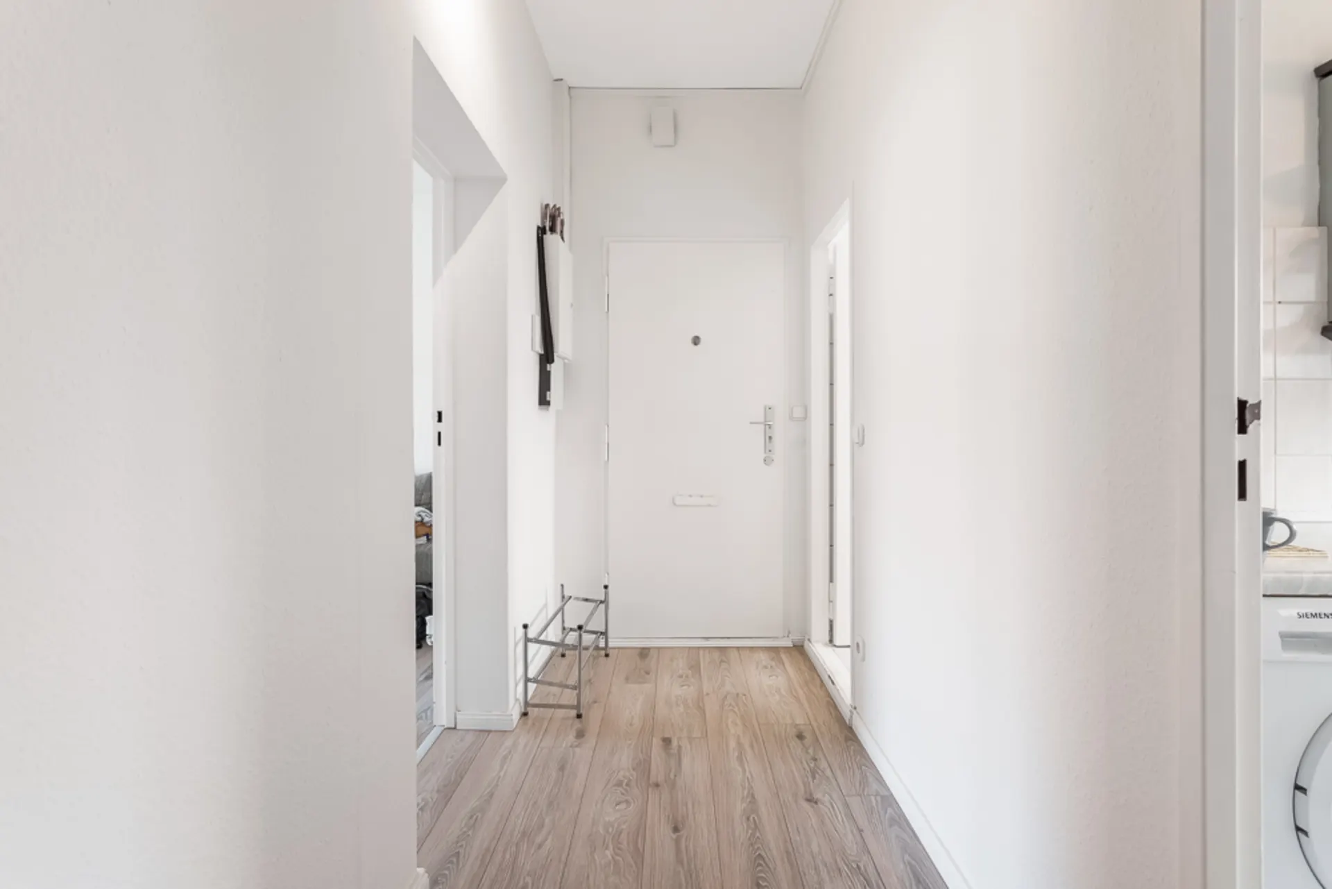 Heller Flur mit Holzboden, weißer Eingangstür und Schuhregal an der Wand.