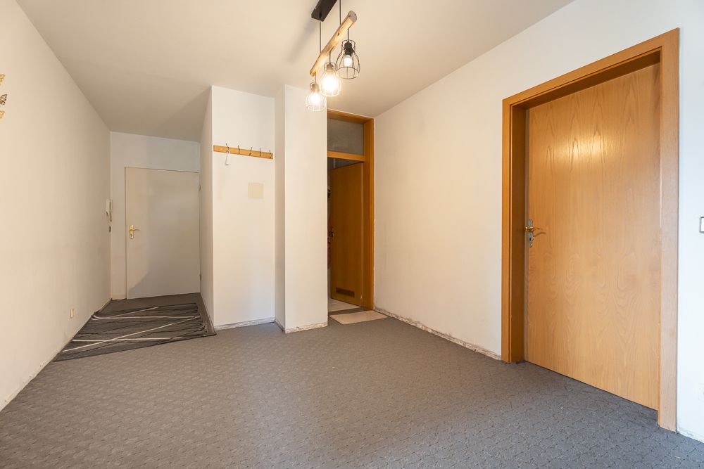 Heller Flur mit Teppichboden, zwei Holztüren und Garderobe an der Wand.