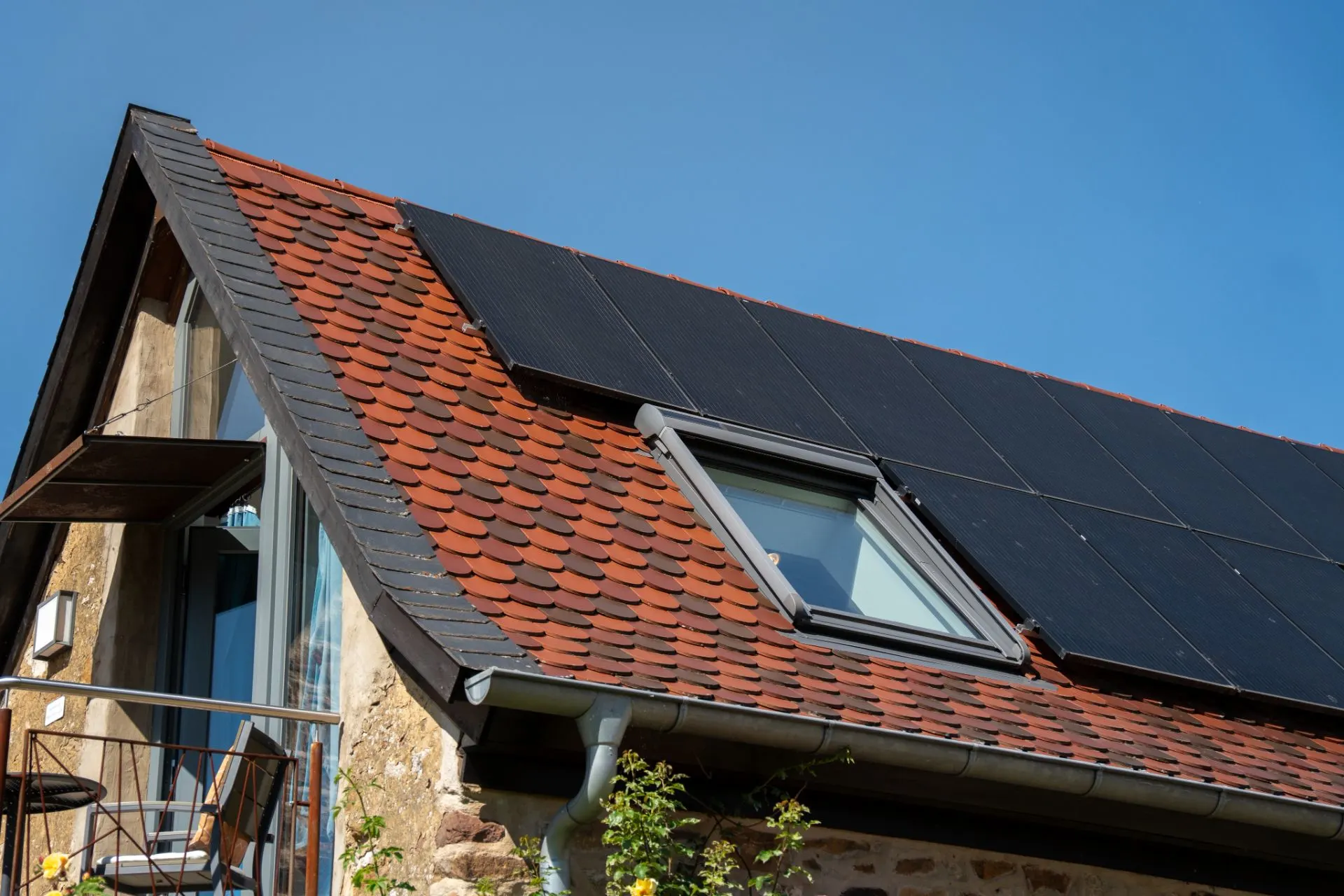 Dach eines Wohnhauses mit roten Ziegeln, Solarpaneelen und einem Dachfenster.