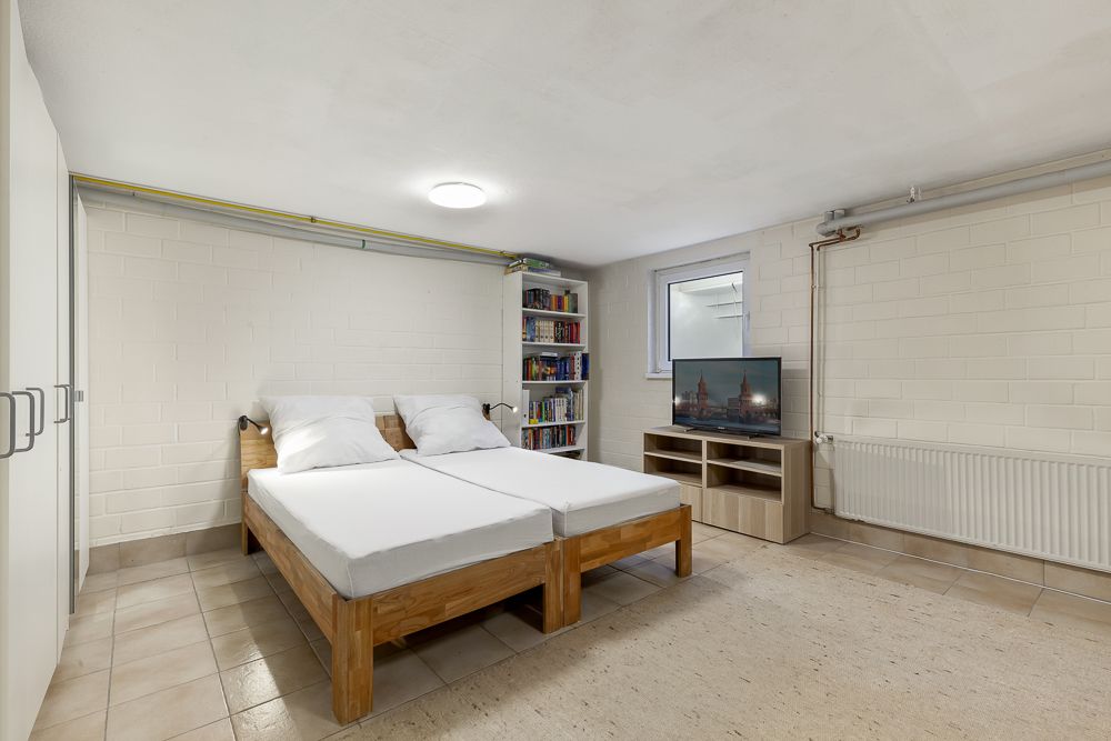 Schlafzimmer mit zwei Einzelbetten, Bücherregal, Fernseher und Fenster im Keller.