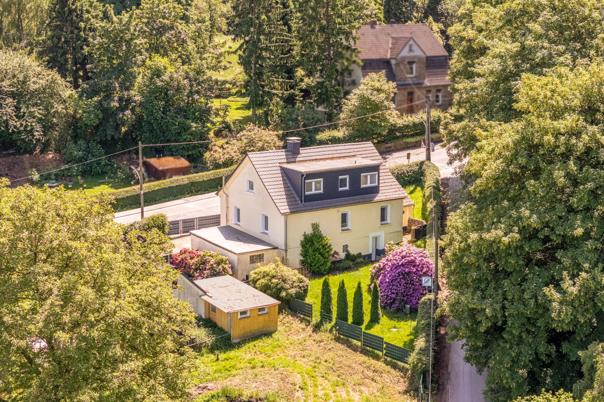 Luftaufnahme eines freistehenden gelben Wohnhauses mit Garten und Nebengebäude.