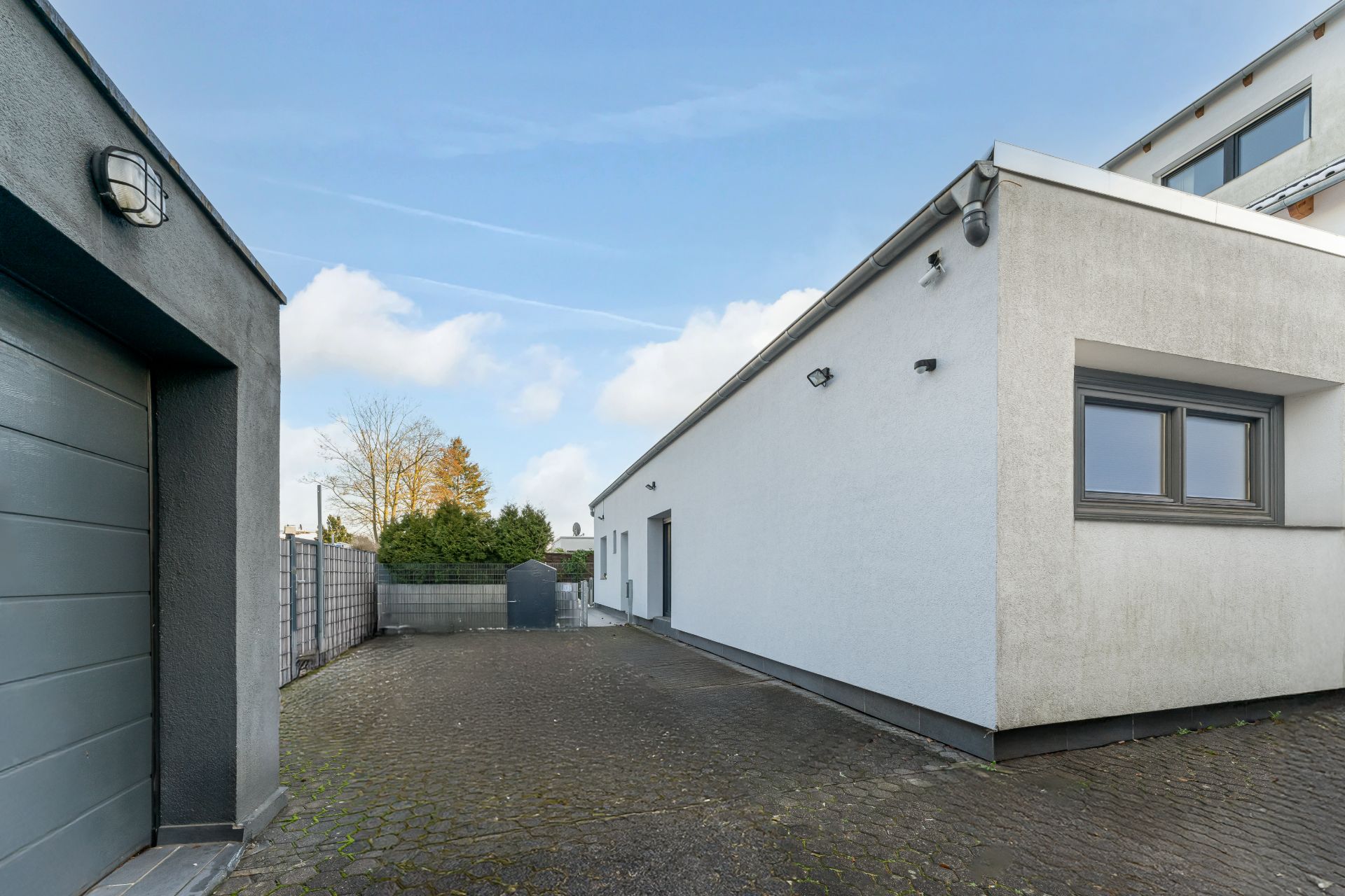 Gepflasterter Hof mit Garage und modernem, weißem Wohnhaus an einem klaren Tag.