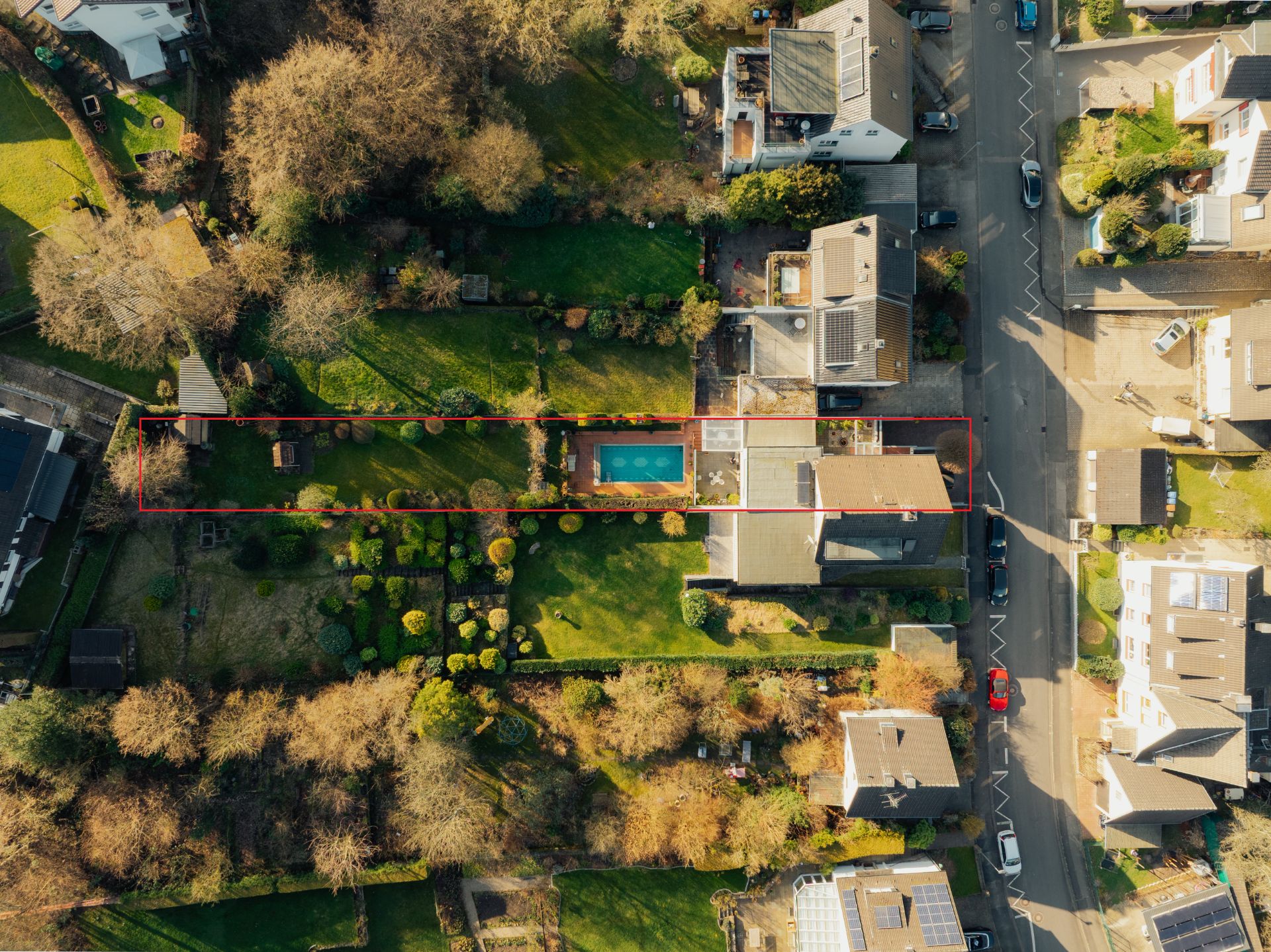 Luftaufnahme eines Hauses mit großem Garten und rechteckigem Pool, von Bäumen umgeben.