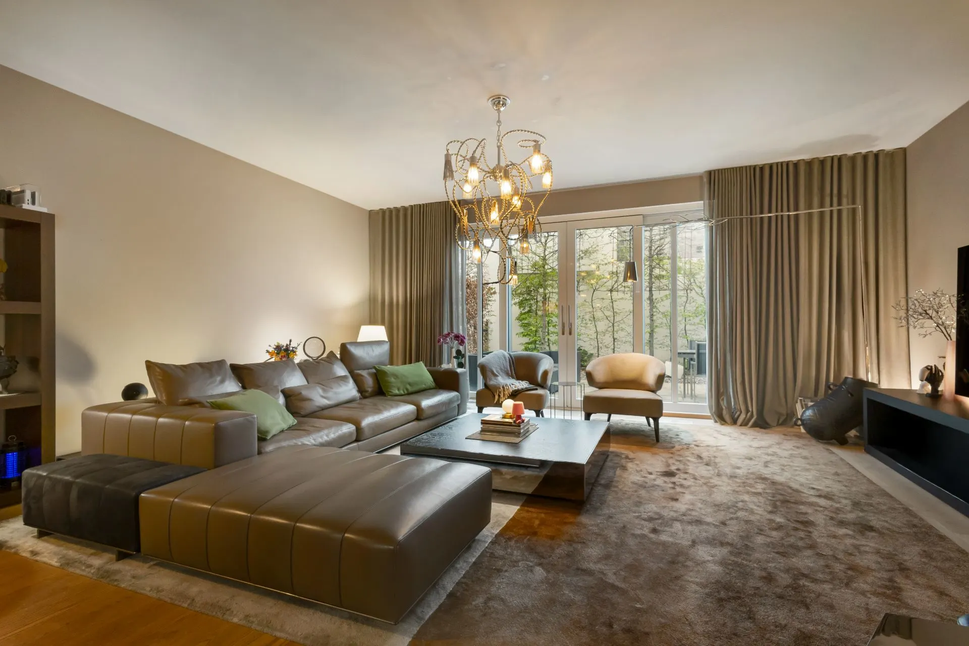 Modernes Wohnzimmer mit großer Ledercouch, Sessel, Couchtisch und großen Fenstern mit Gardinen.