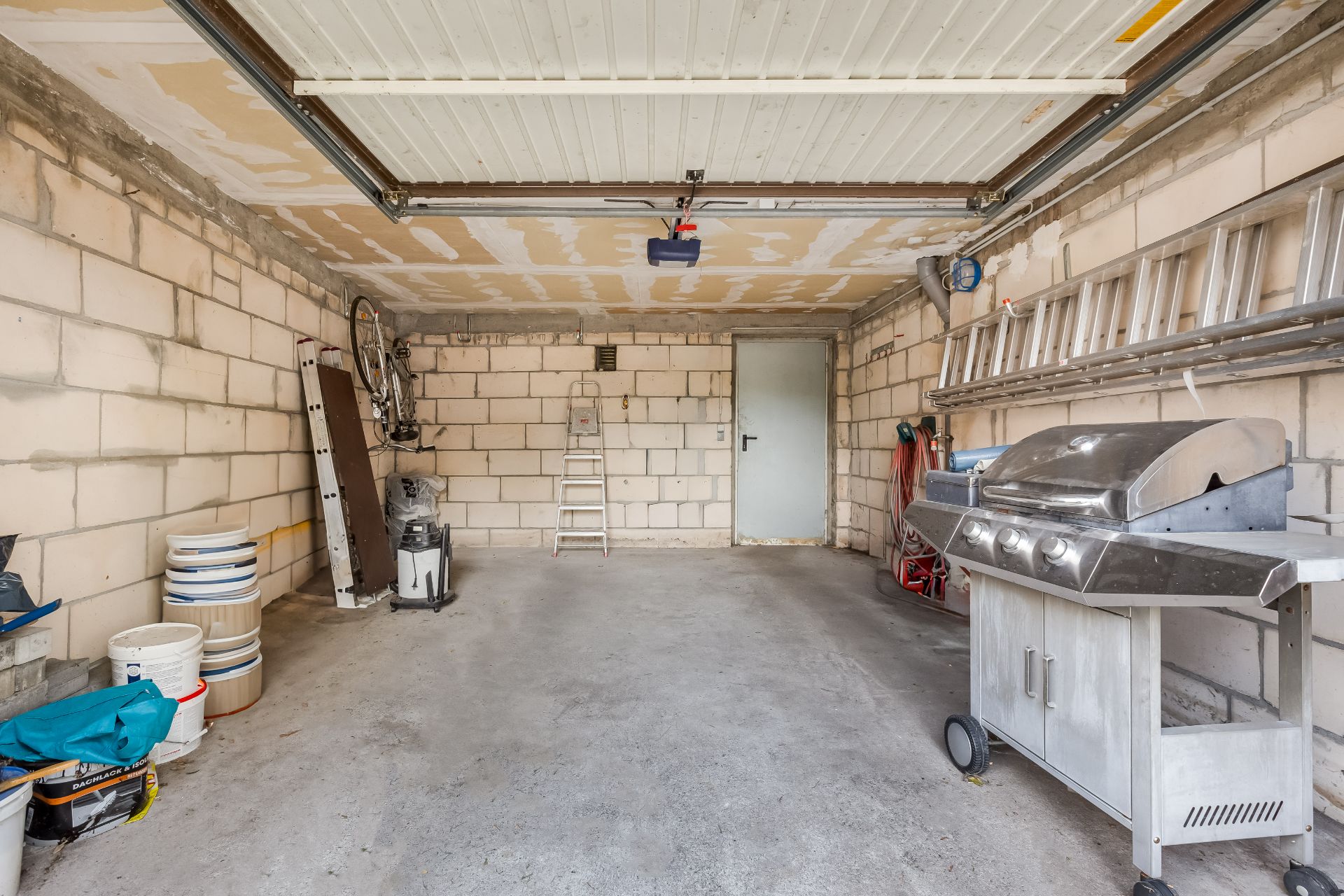 Garage mit Grill, Leitern, Farbbehältern und Werkzeugen an den Wänden.