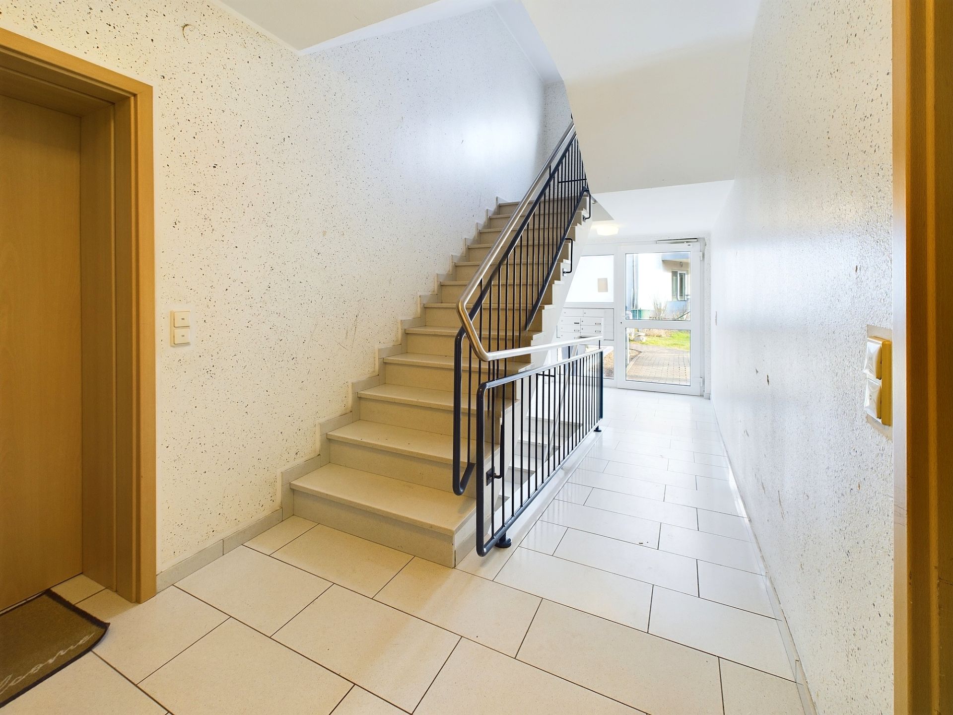 Heller Hausflur mit Treppe nach oben und Glastür zum Außenbereich.