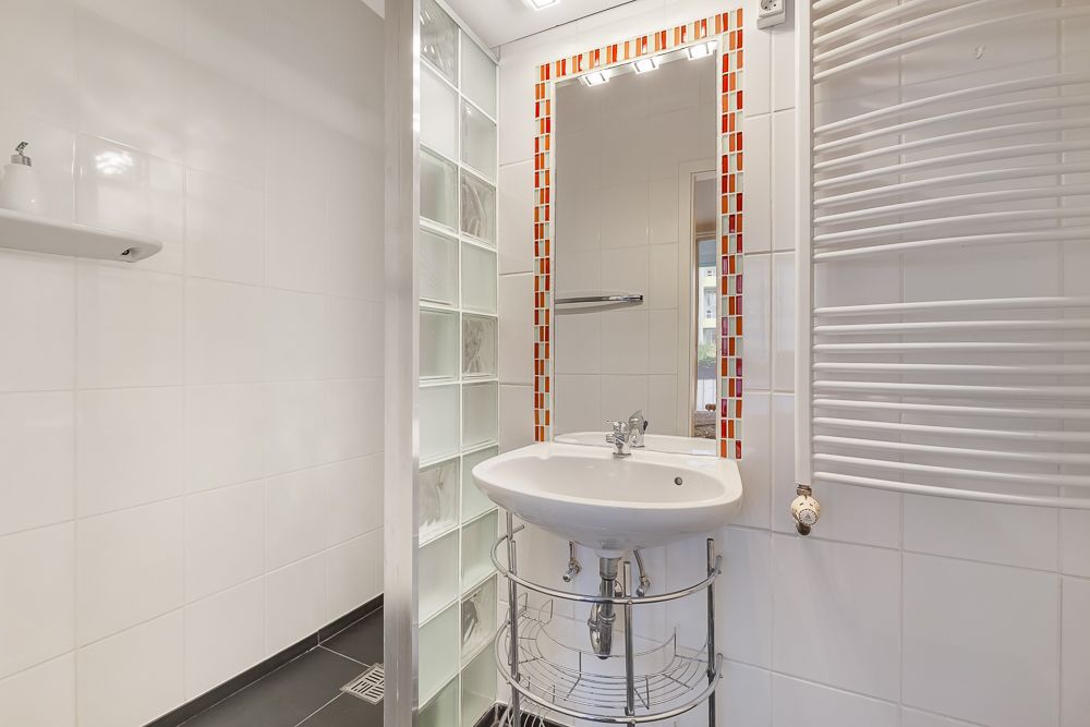 Modernes Badezimmer mit Waschbecken, Spiegel mit roten Fliesen und Handtuchheizkörper.