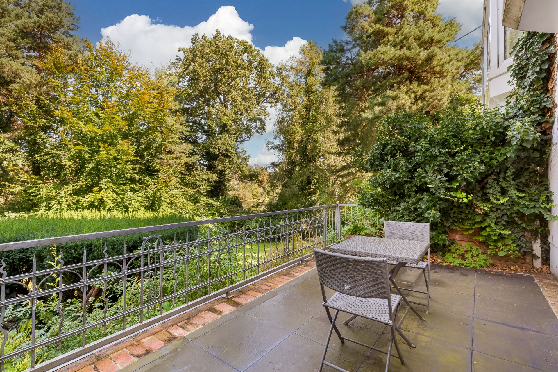 Terrasse mit zwei Stühlen und Tisch, Ausblick auf Garten mit vielen Bäumen.