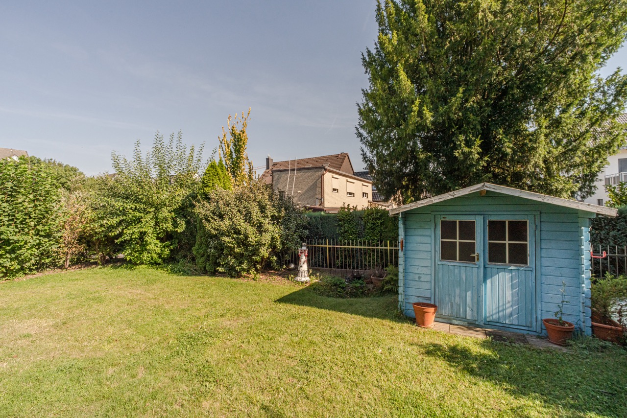 Garten mit einer kleinen blauen Holzhütte und viel Grün rundherum.