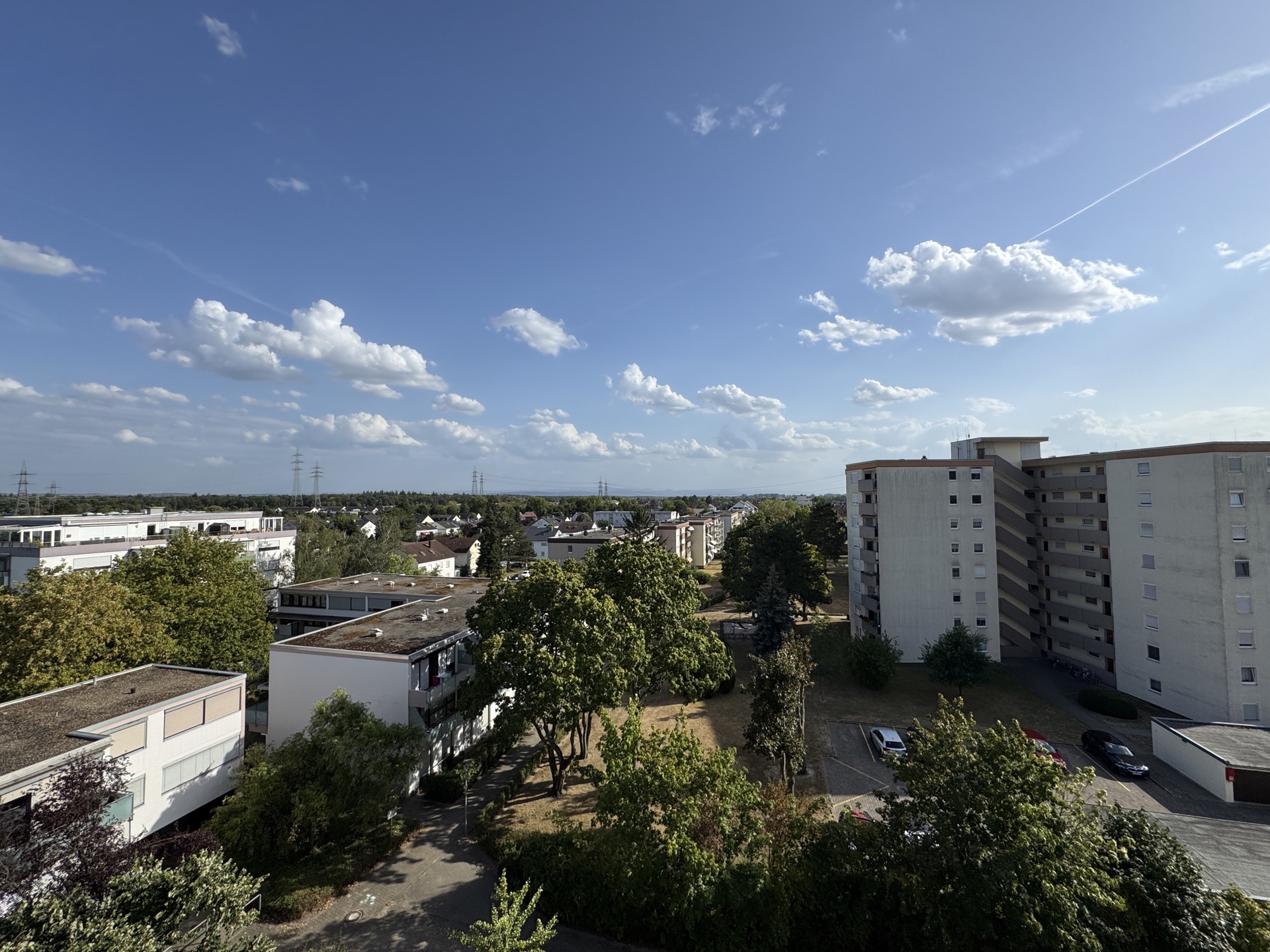 Blick auf Wohngebäude, Bäume und geparkte Autos unter blauem Himmel mit Wolken.