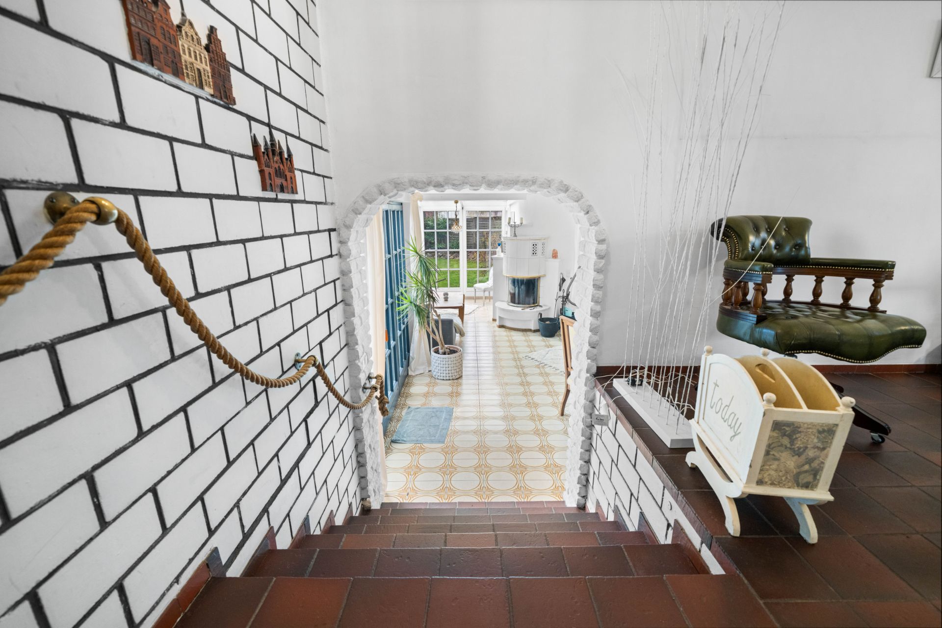 Treppe mit Seilgeländer führt zu einem hellen Wohnraum mit Kamin und Pflanzen.