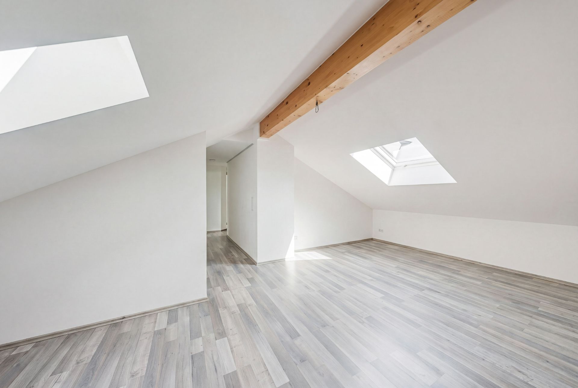 Heller Dachraum mit schrägen Wänden, Holzbalken, zwei Dachfenstern und Laminatboden.