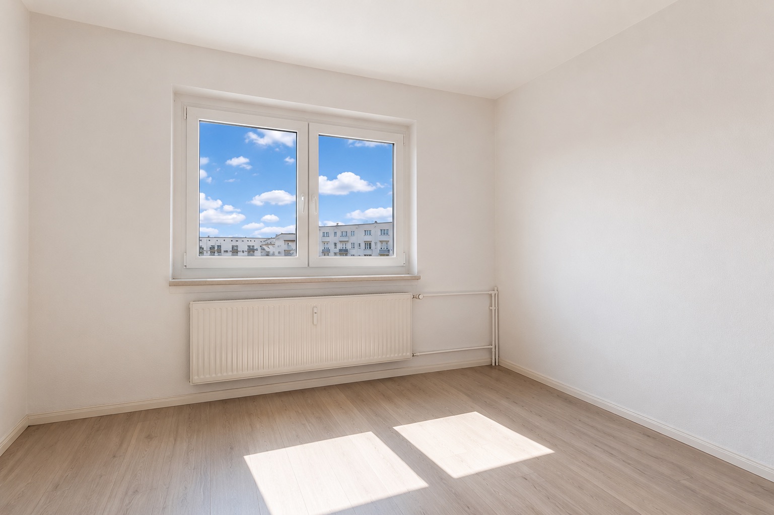 Leeres, helles Zimmer mit großem Fenster, Heizkörper und hellem Holzboden.