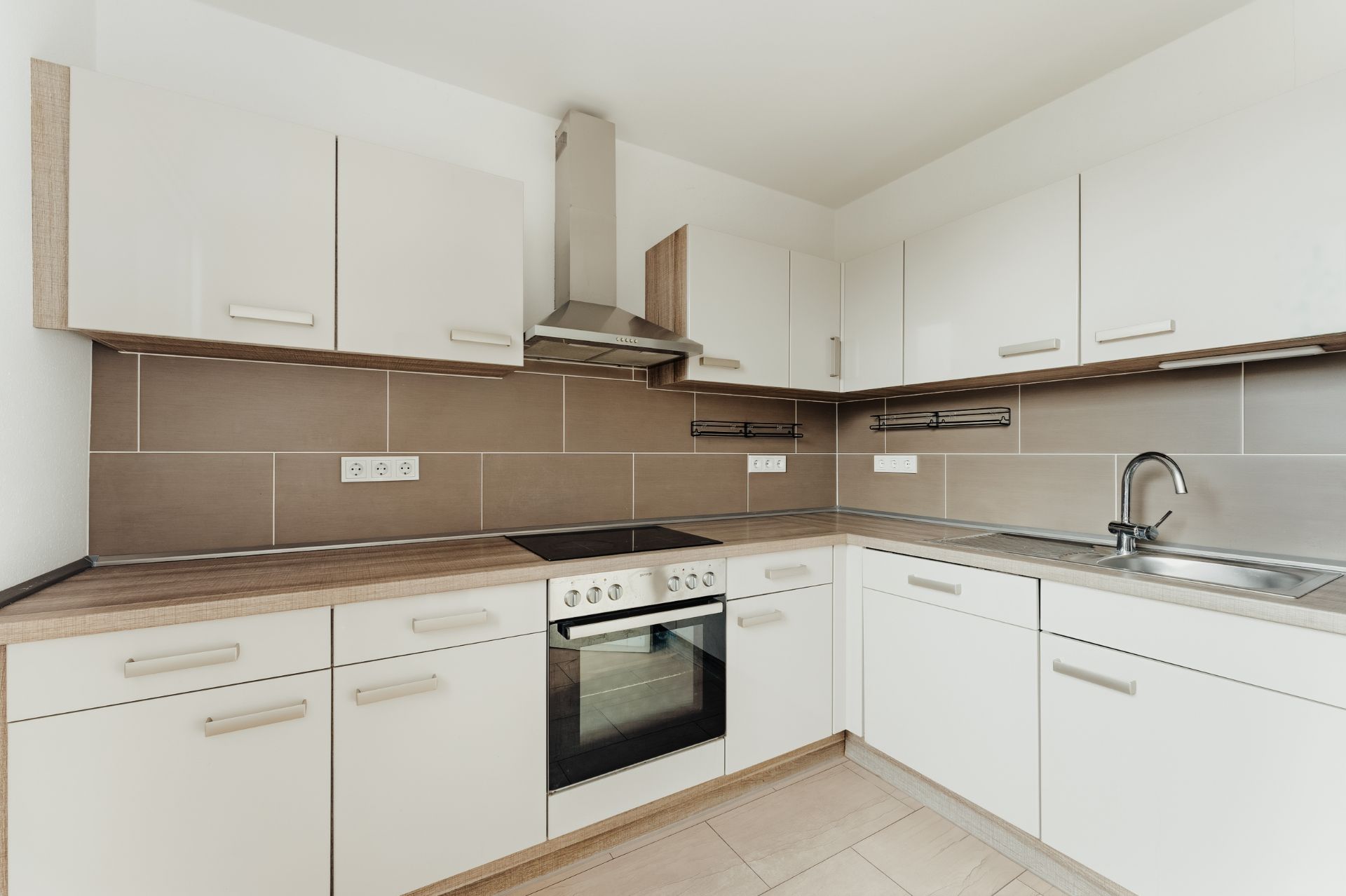 Moderne Küche mit weißen Schränken, Herd, Backofen und Edelstahlspüle.