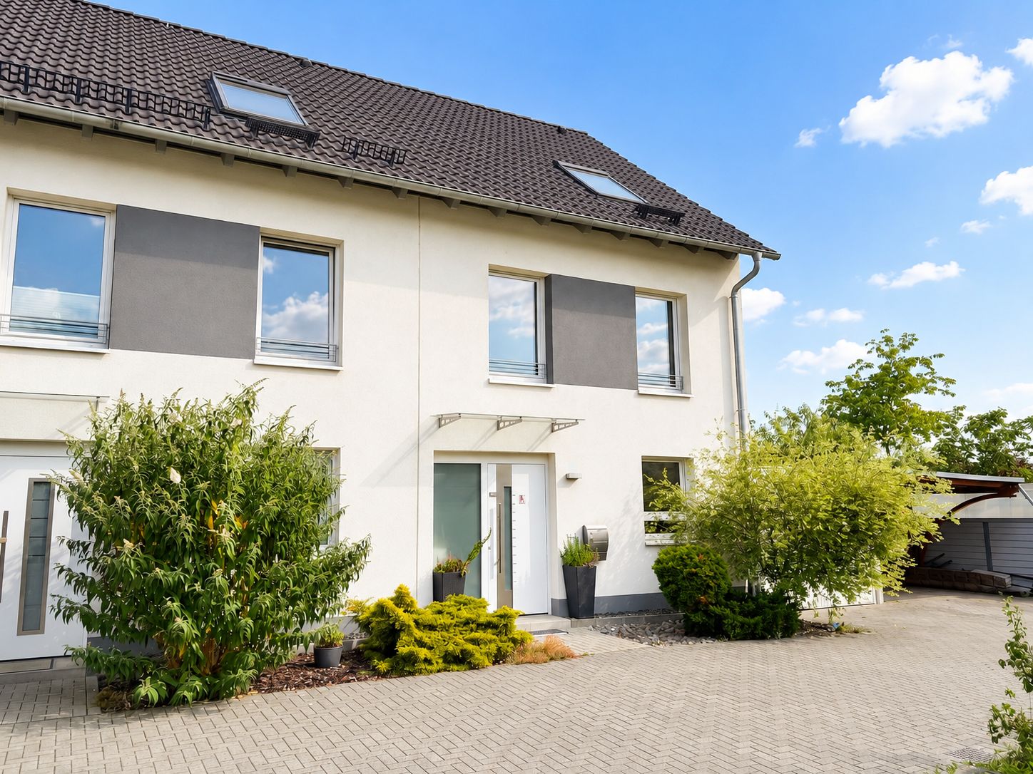 Zweistöckiges Wohnhaus mit dunklem Dach, großen Fenstern und bepflanztem Vorgarten.