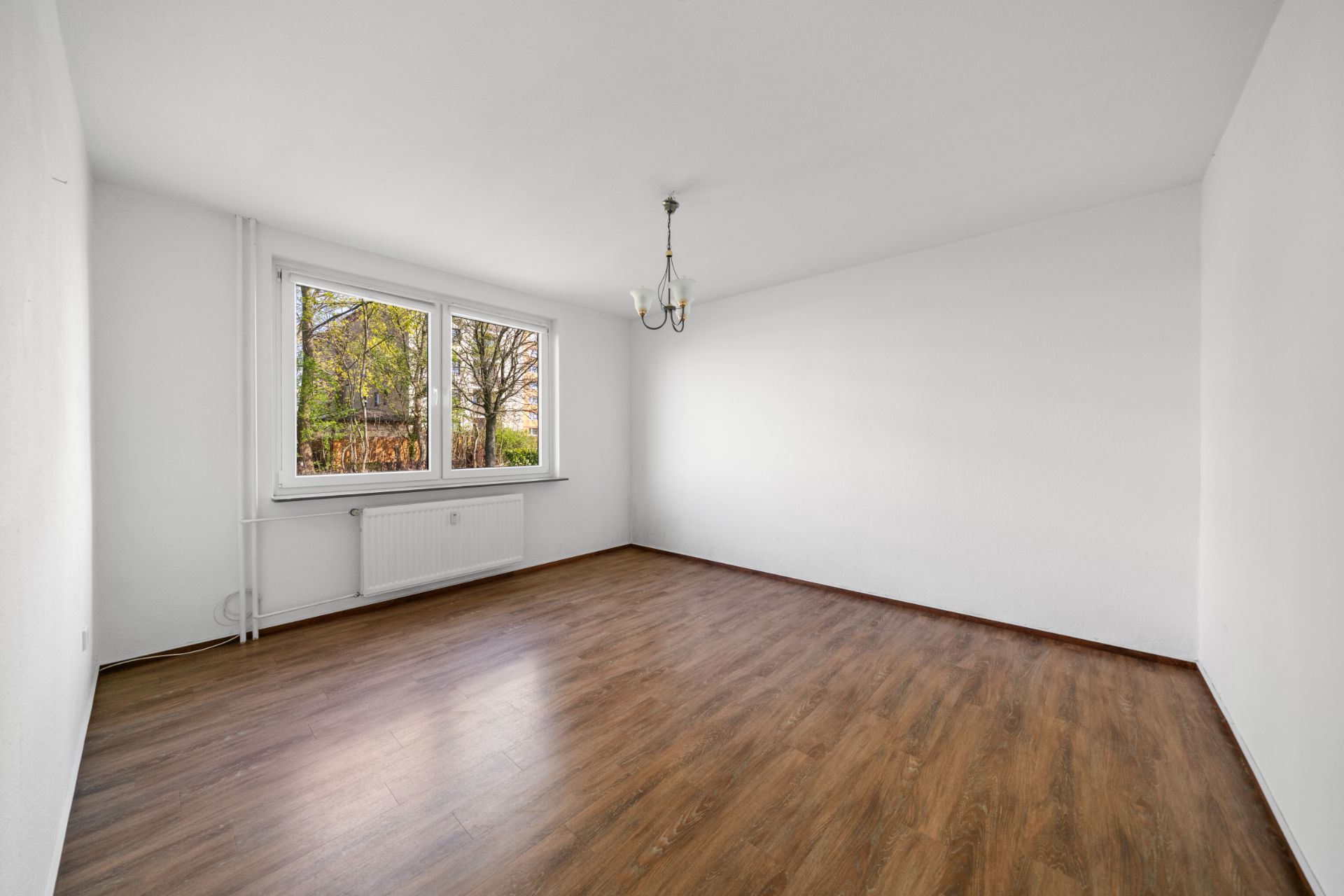Leerer Raum mit Holzfußboden, weiß gestrichenen Wänden und großem Fenster.